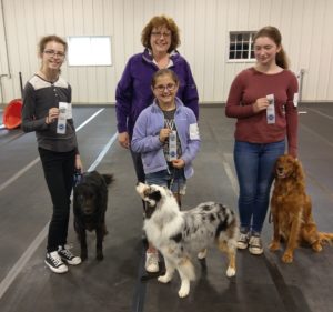 Three 4-H members with their dogs holding their AKC ribbons.